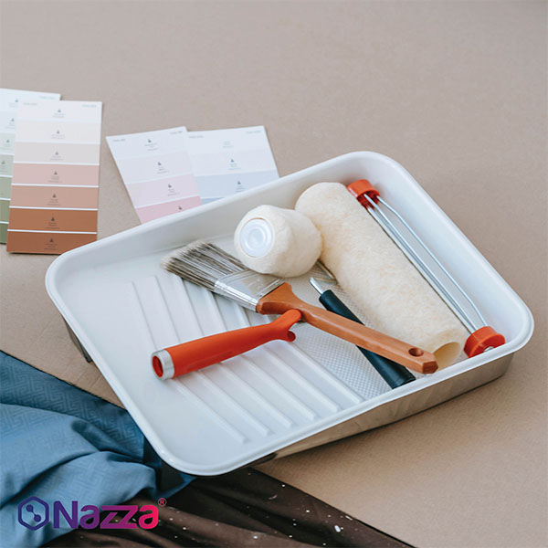 Bandeja de pintura con rodillos, brochas y accesorios preparados para realizar trabajos de pintura en paredes interiores.